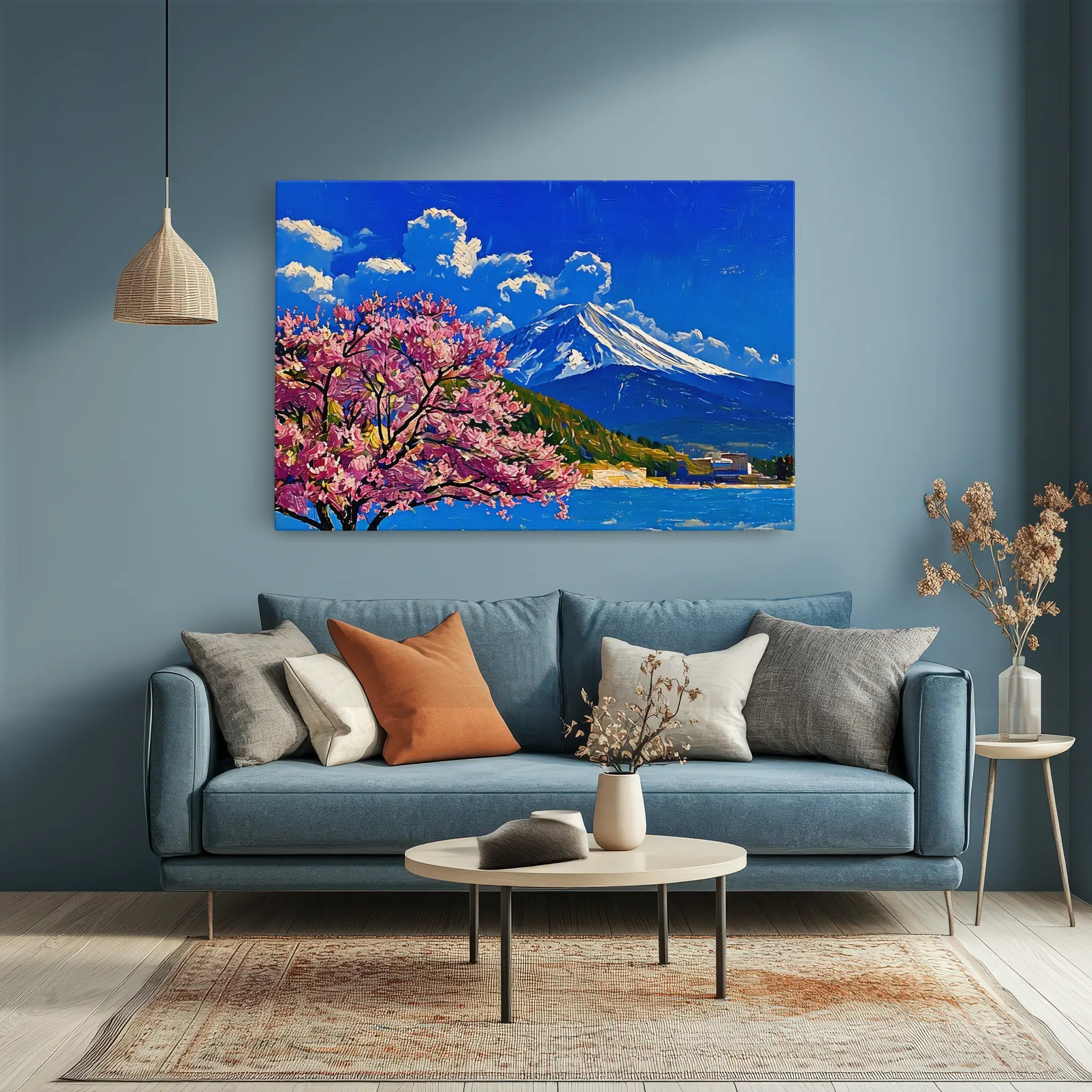 A cozy living room with a blue sofa, assorted pillows, a round coffee table, and a vibrant painting of a mountain and cherry blossoms on the wall.